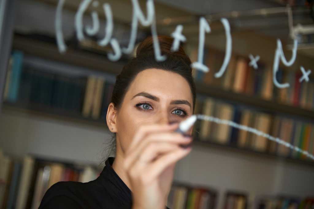 Female business leader in Blockchain technology writing down a mathematical formula on glass in a library